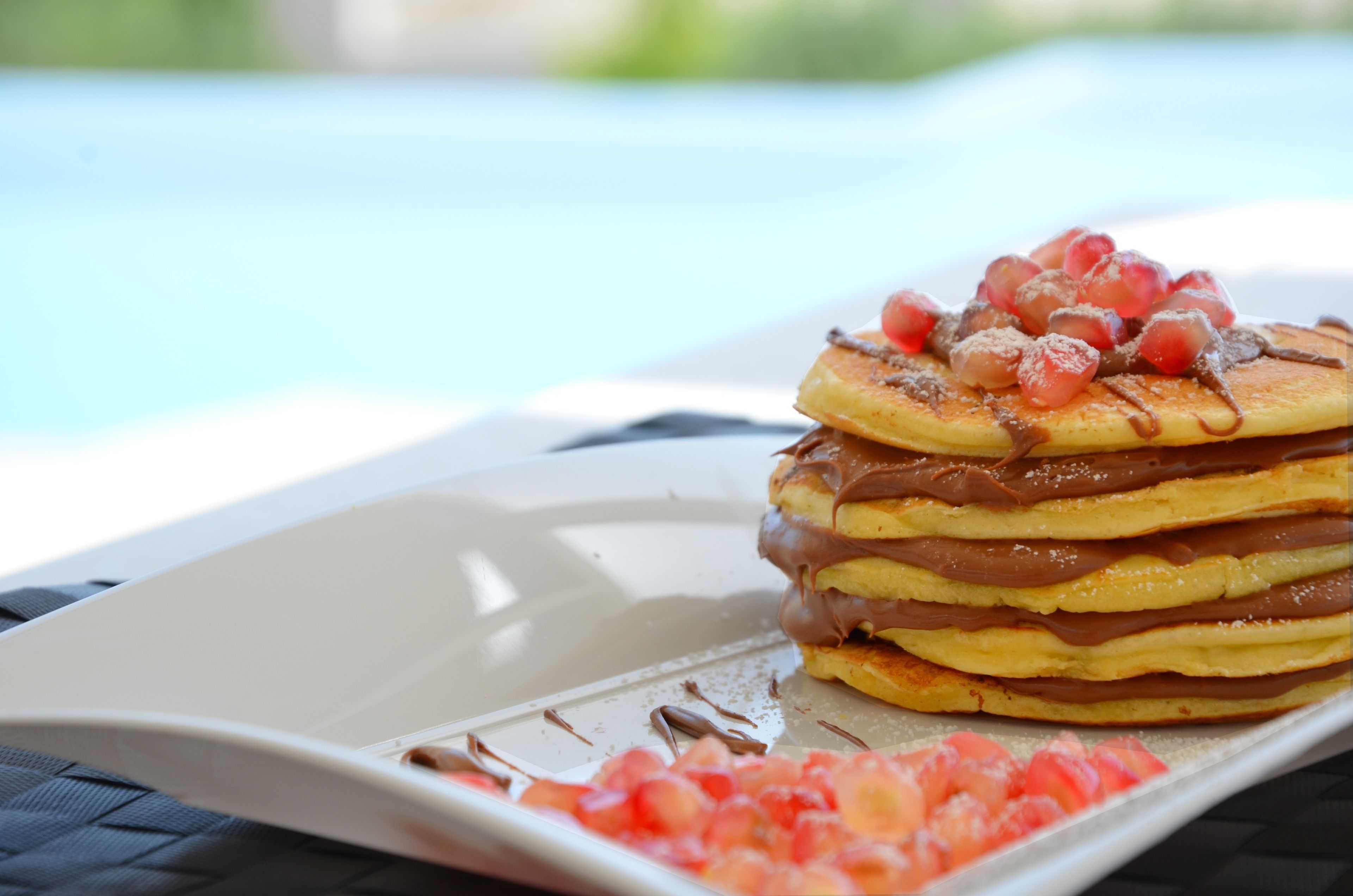 Una pila de tortitas con crema de chocolate y fruta sobre un plato blanco.