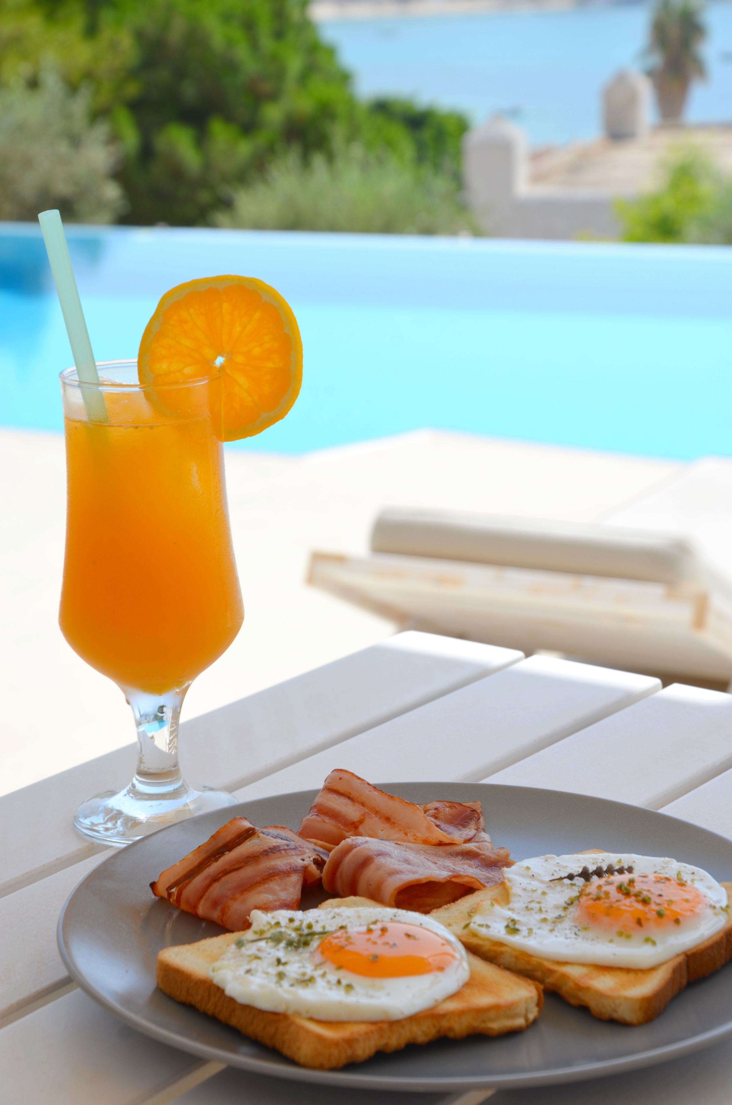 A breakfast plate with toast, eggs, and bacon, and a glass of orange juice with a straw and an orange slice.