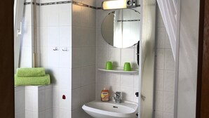 Un baño con lavamanos blanco, espejo, cortina de ducha y toalla verde.
