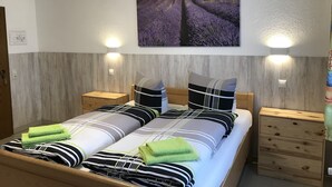 Una cama doble con ropa de cama a rayas, dos mesitas de noche, un cuadro colgado en la pared de campos de lavanda y dos lámparas de pared.