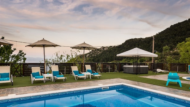 A swimming pool with lounge chairs and umbrellas, surrounded by a landscaped area and a hilly backdrop. - Ilaeira Mountain Resort (Sparta)