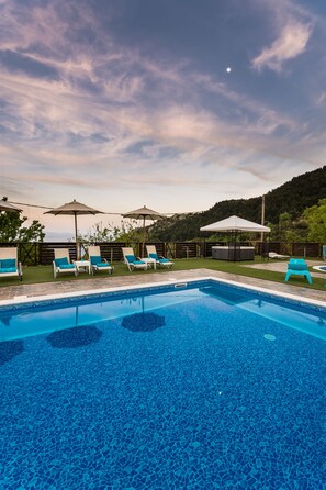 A swimming pool with lounge chairs and umbrellas, surrounded by a landscaped area and a hilly backdrop.