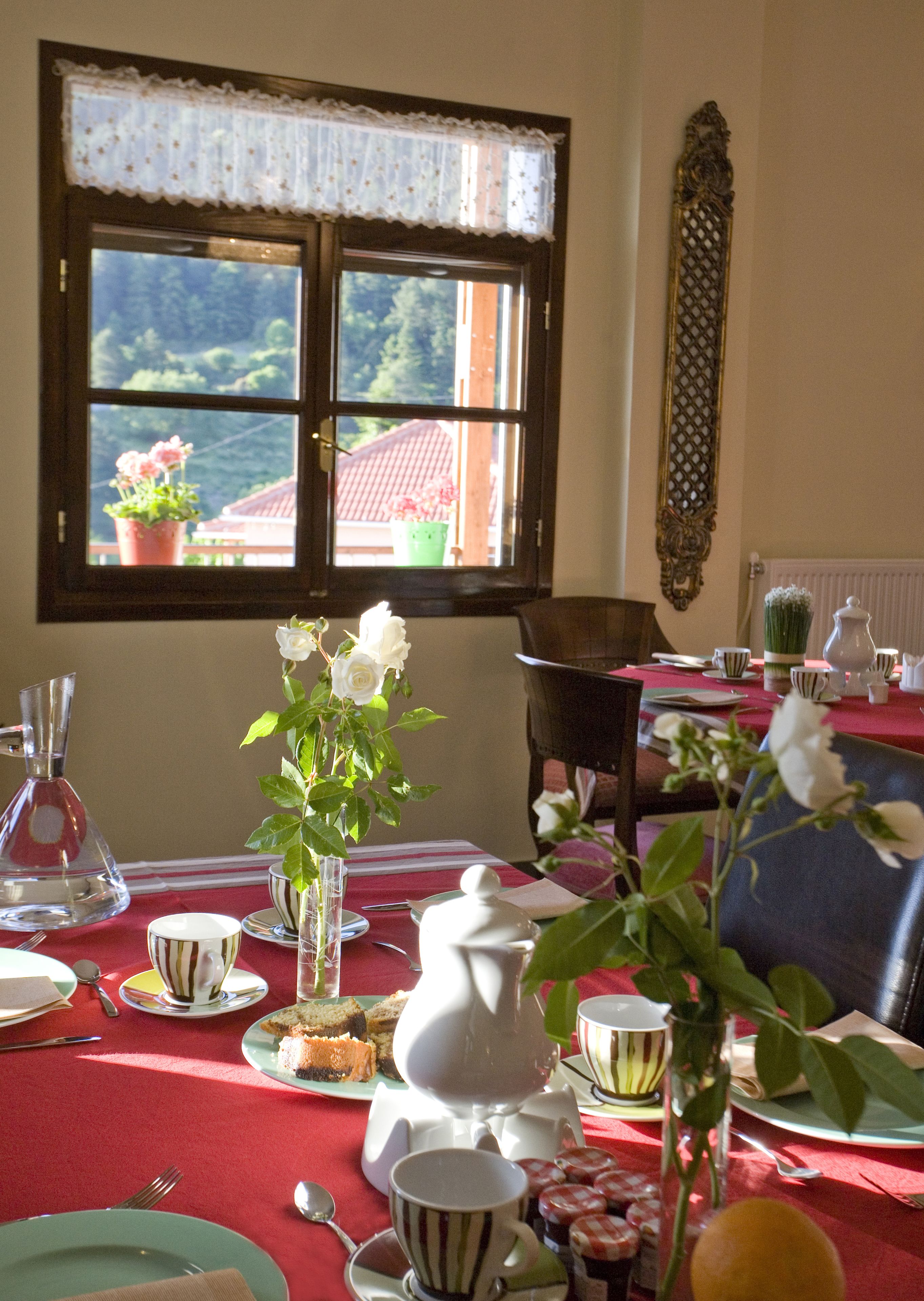 A dining table set with a red tablecloth, white teapot, and striped cups.