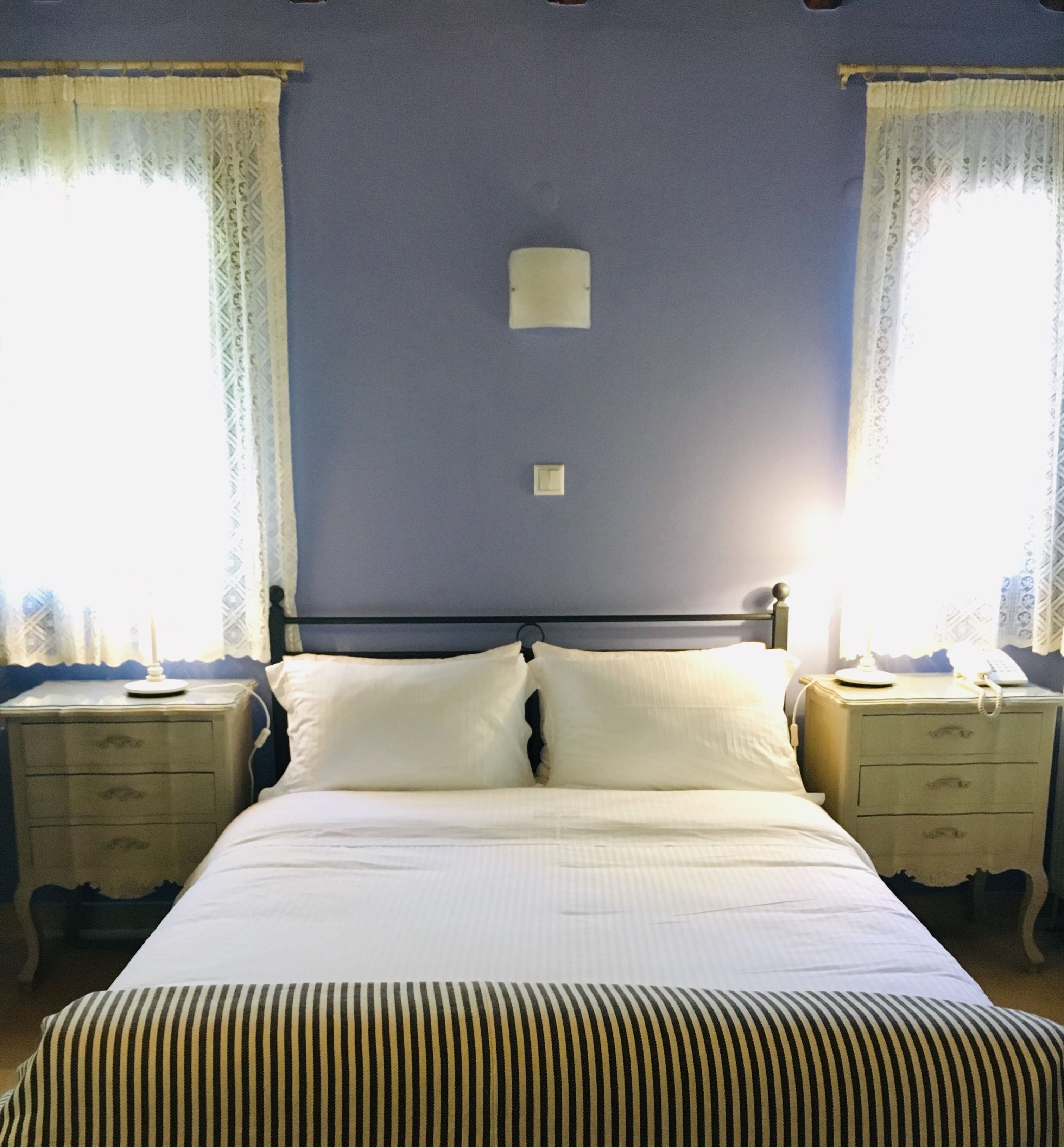 A bedroom with a bed, two bedside tables, a nightstand, a wall-mounted light, and curtains.