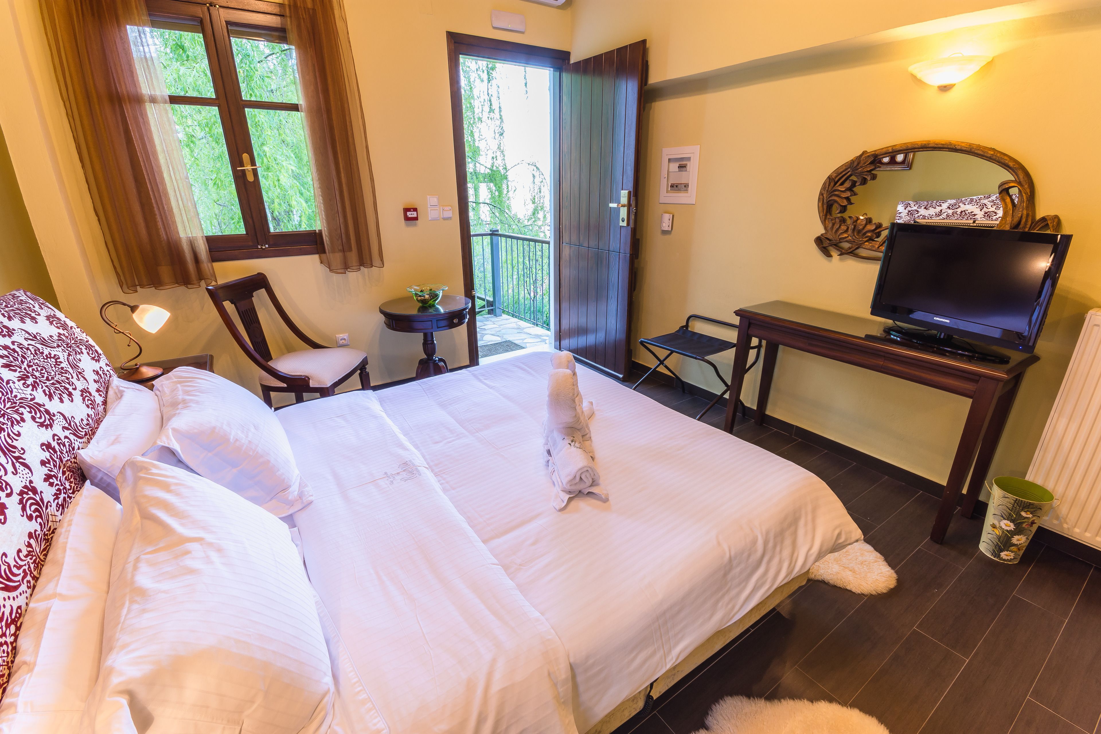 A hotel room with a bed, a desk with a television, a chair, a small table, and a window with curtains.