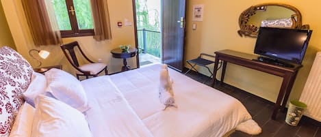 Ein Hotelzimmer mit einem Bett, einem Schreibtisch mit Fernseher, einem Sessel, einem kleinen Tisch und einem Fenster mit Vorhängen.