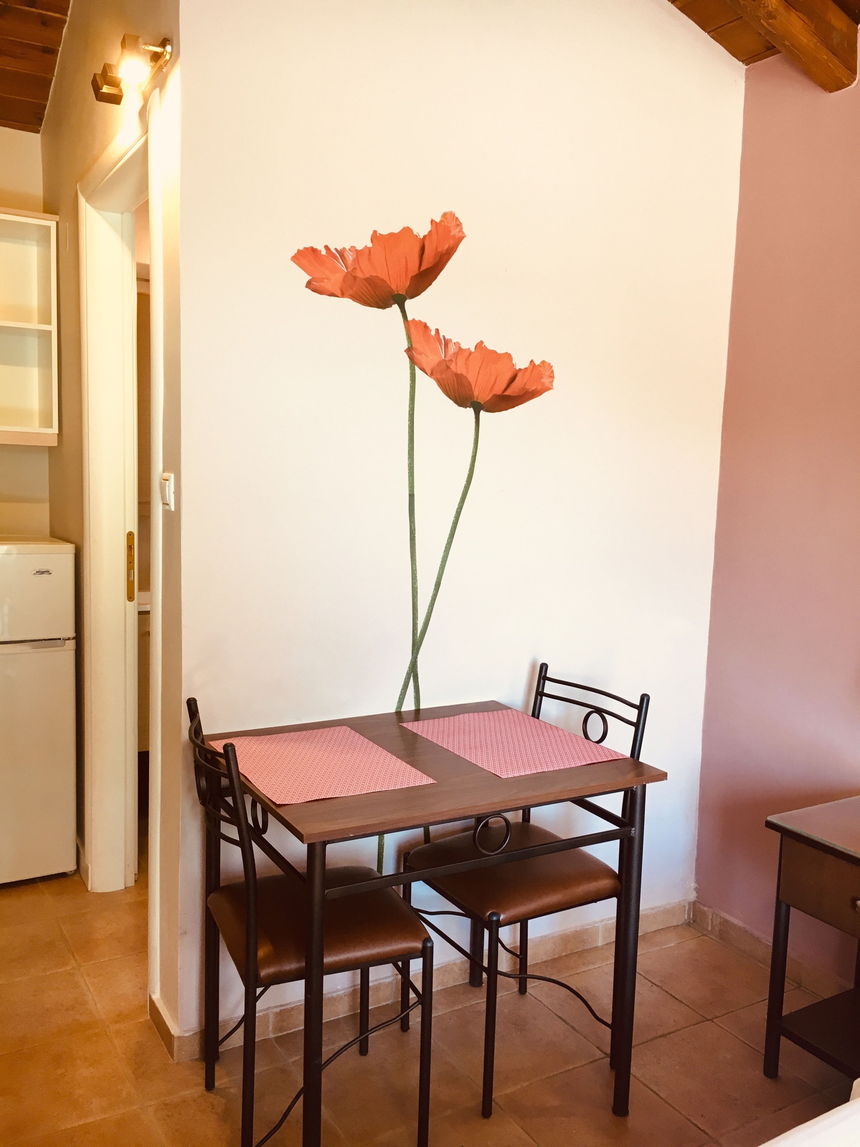 Uma área de refeições com uma mesa de madeira e quatro cadeiras, duas com jogos americanos cor-de-rosa.