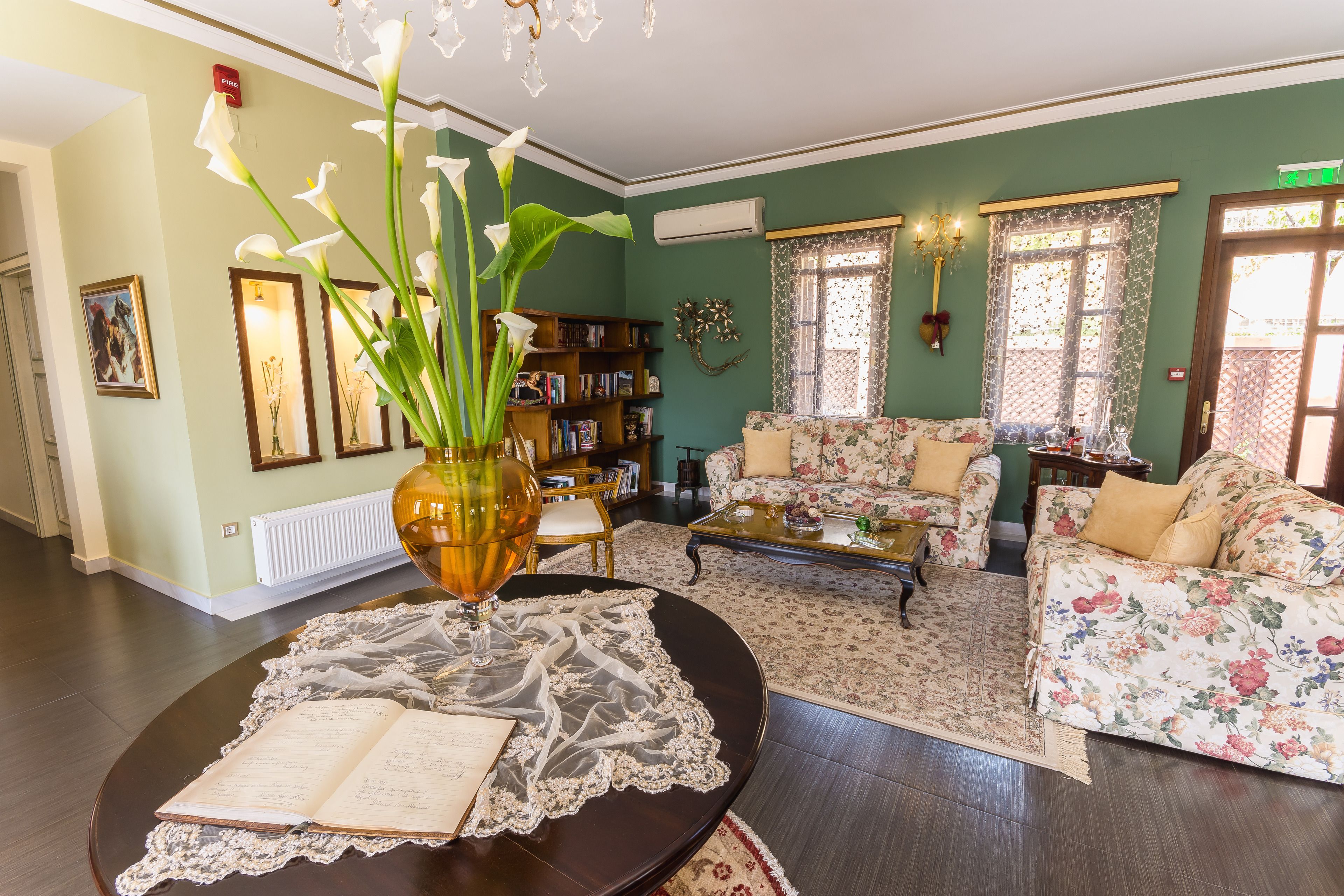 A living room with a sofa, a coffee table, and a bookshelf. There is a vase with flowers on a table.