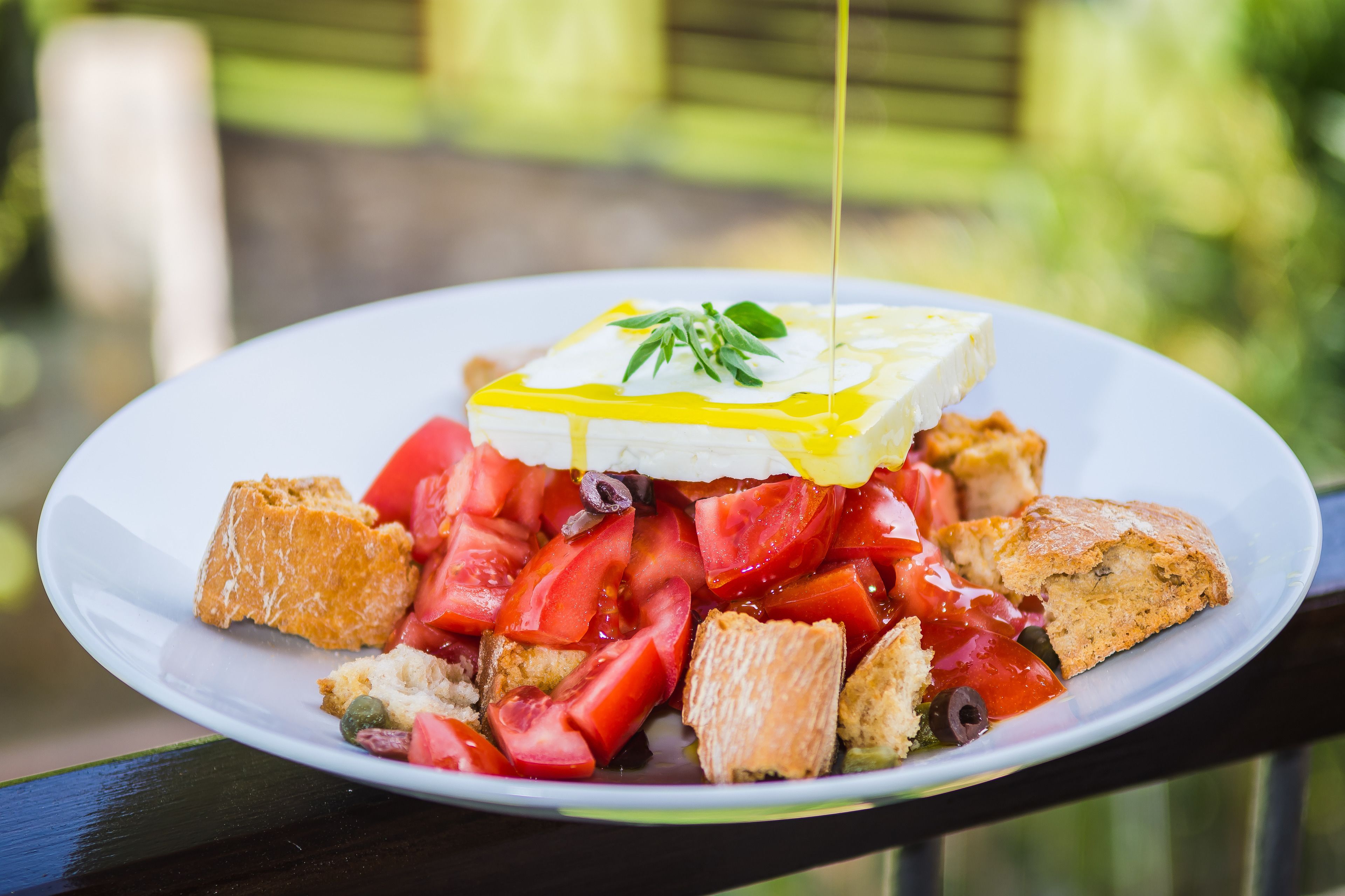 Une assiette de nourriture composée de tomates, d’olives et de pain, agrémentée d’une cuillerée de crème et d’une branche d’herbes aromatiques.