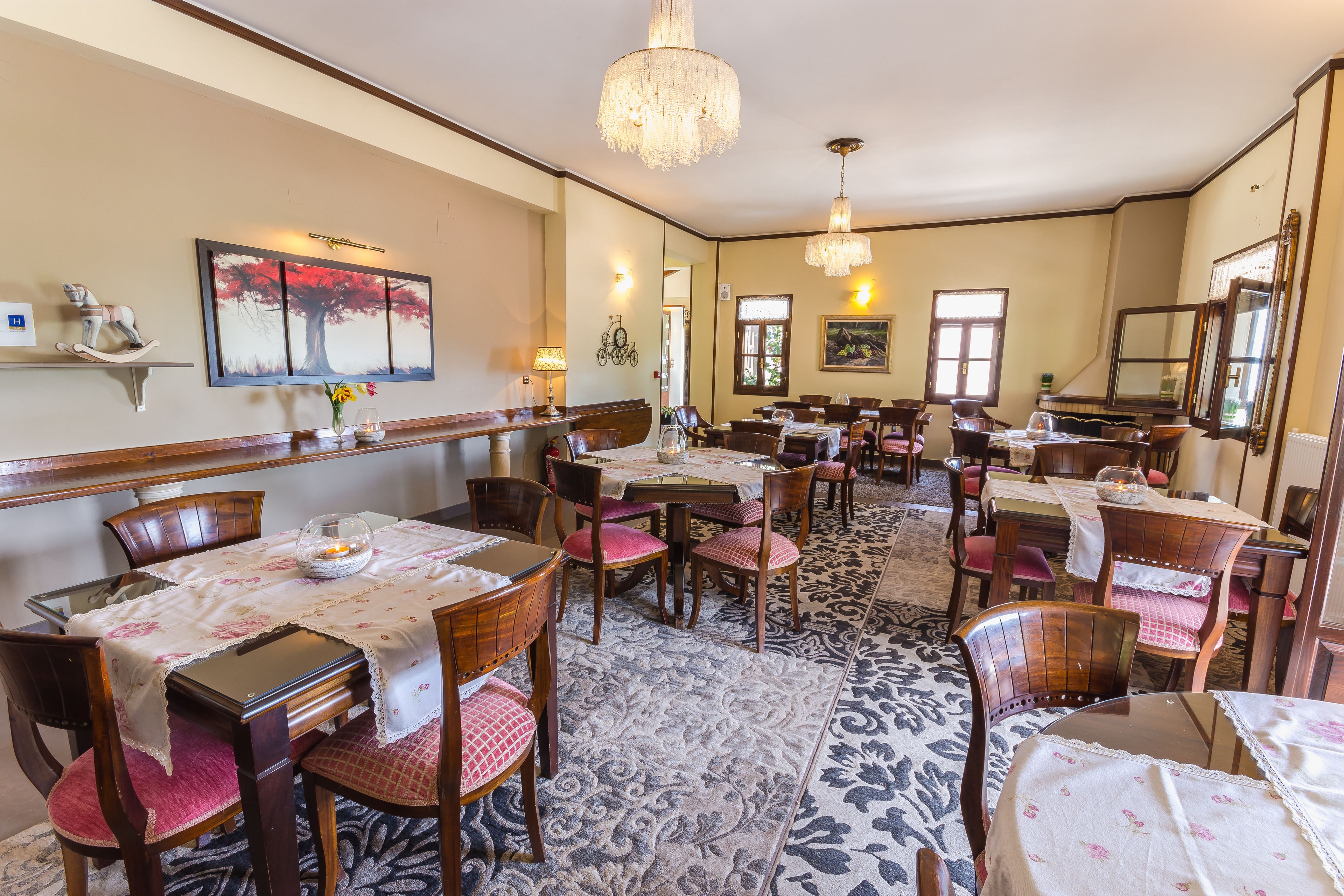 A dining area with multiple tables and chairs, chandeliers, and wall-mounted artwork.