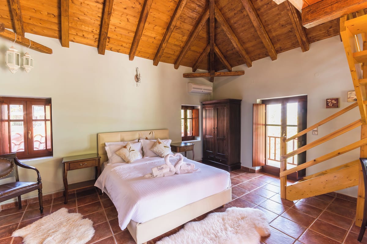 Ein Schlafzimmer mit Holzboden, einem Bett mit weißer Bettwäsche, einem Holzstuhl, einem kleinen Tisch und einer Treppe.