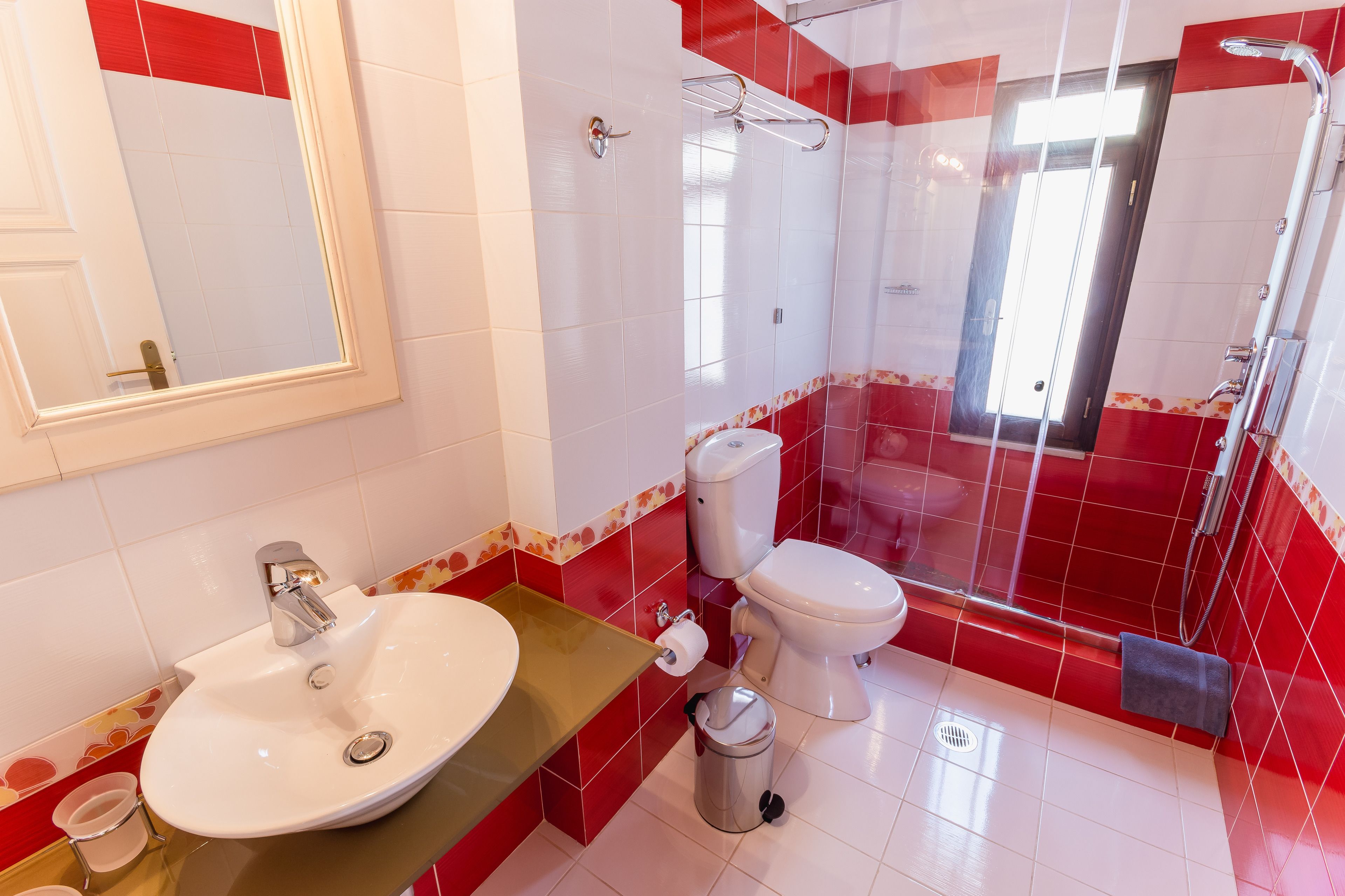 Een badkamer met een wit wastafel, rode betegelde wanden, een toilet en een douchehoek.