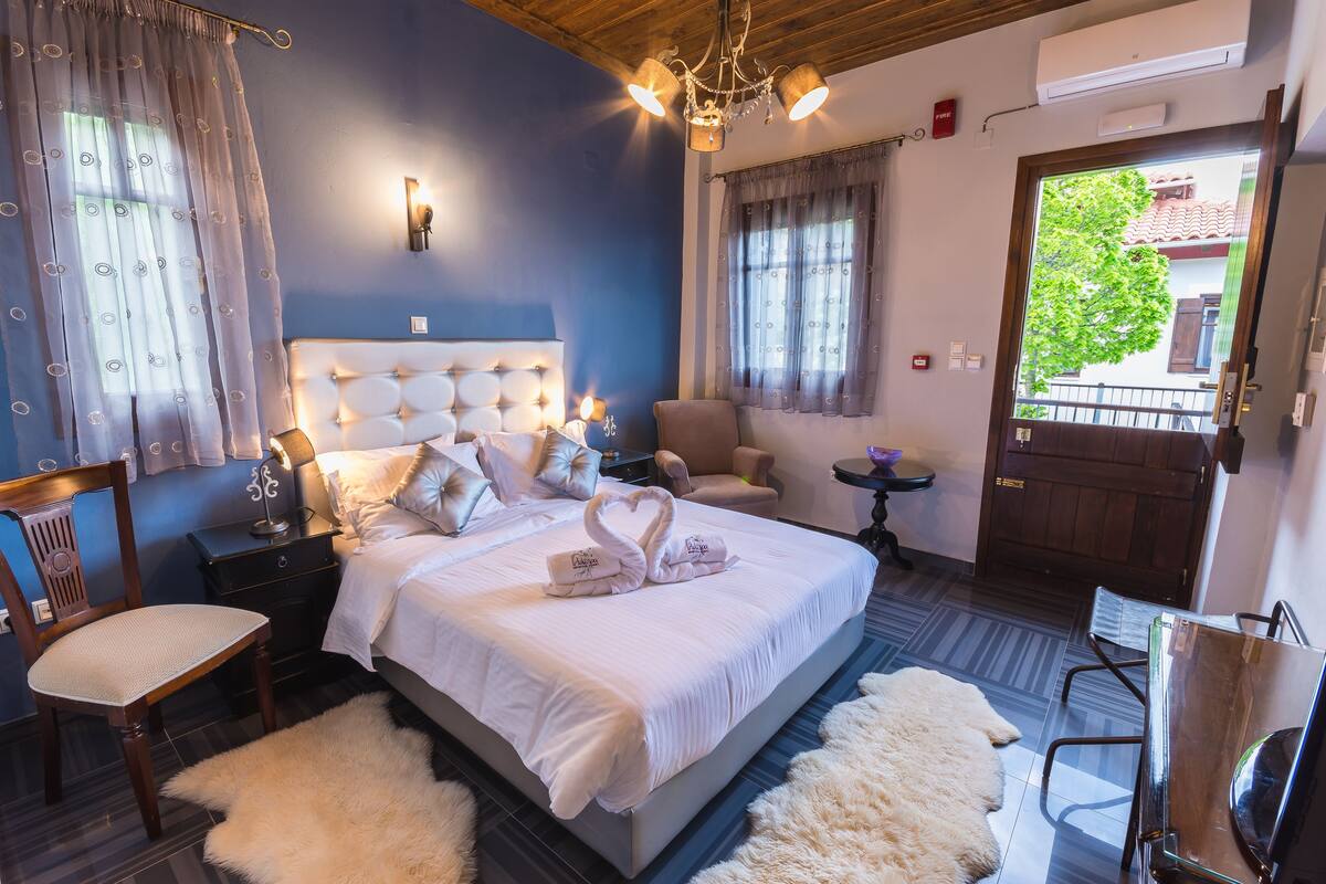 Ein Schlafzimmer mit einem großen Bett, einem Sessel, einem kleinen Tisch und Blick ins Freie.