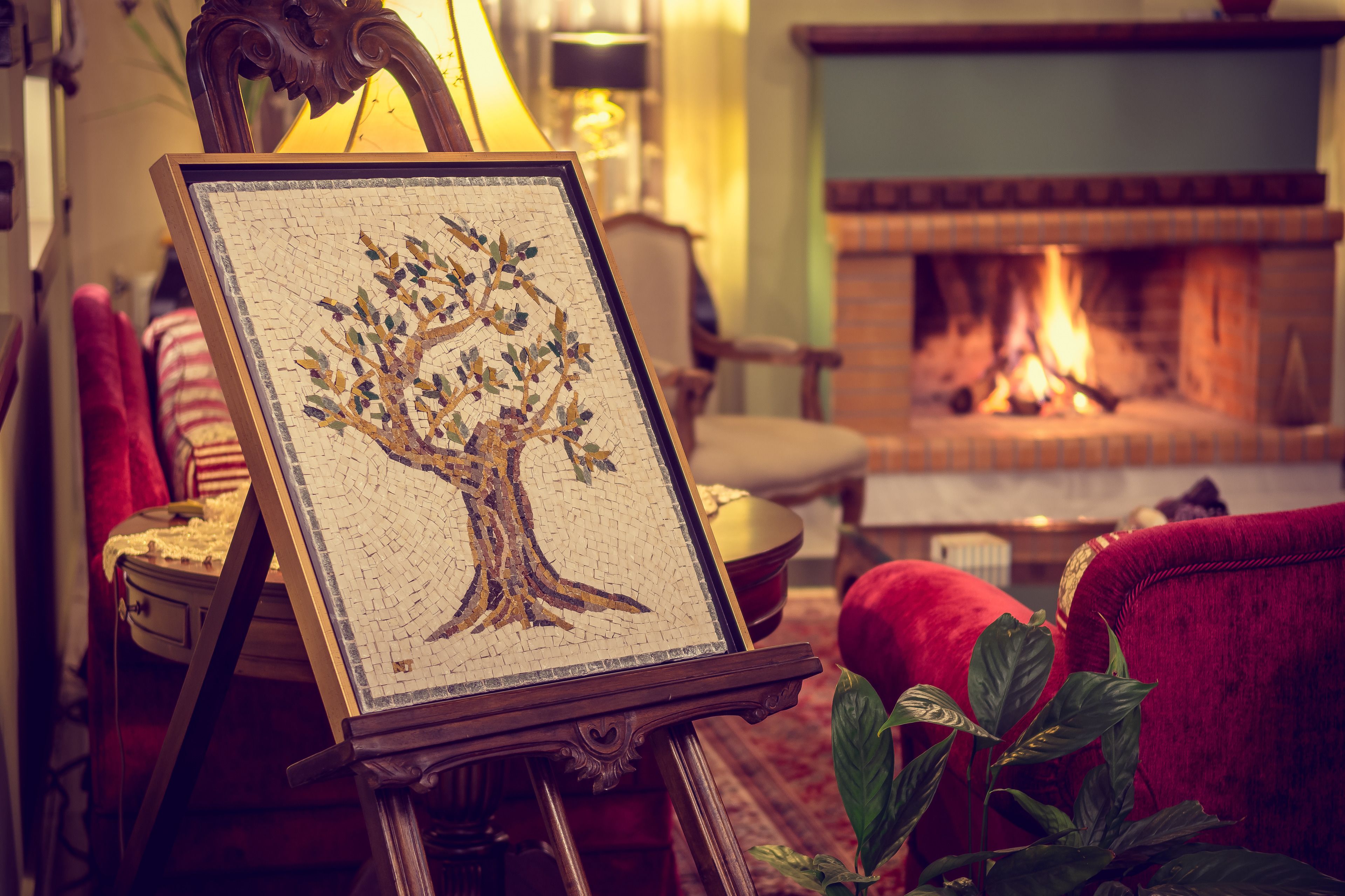 Una obra de arte en mosaico con forma de árbol, enmarco, sobre un caballete en un salón acogedor con chimenea al fondo.