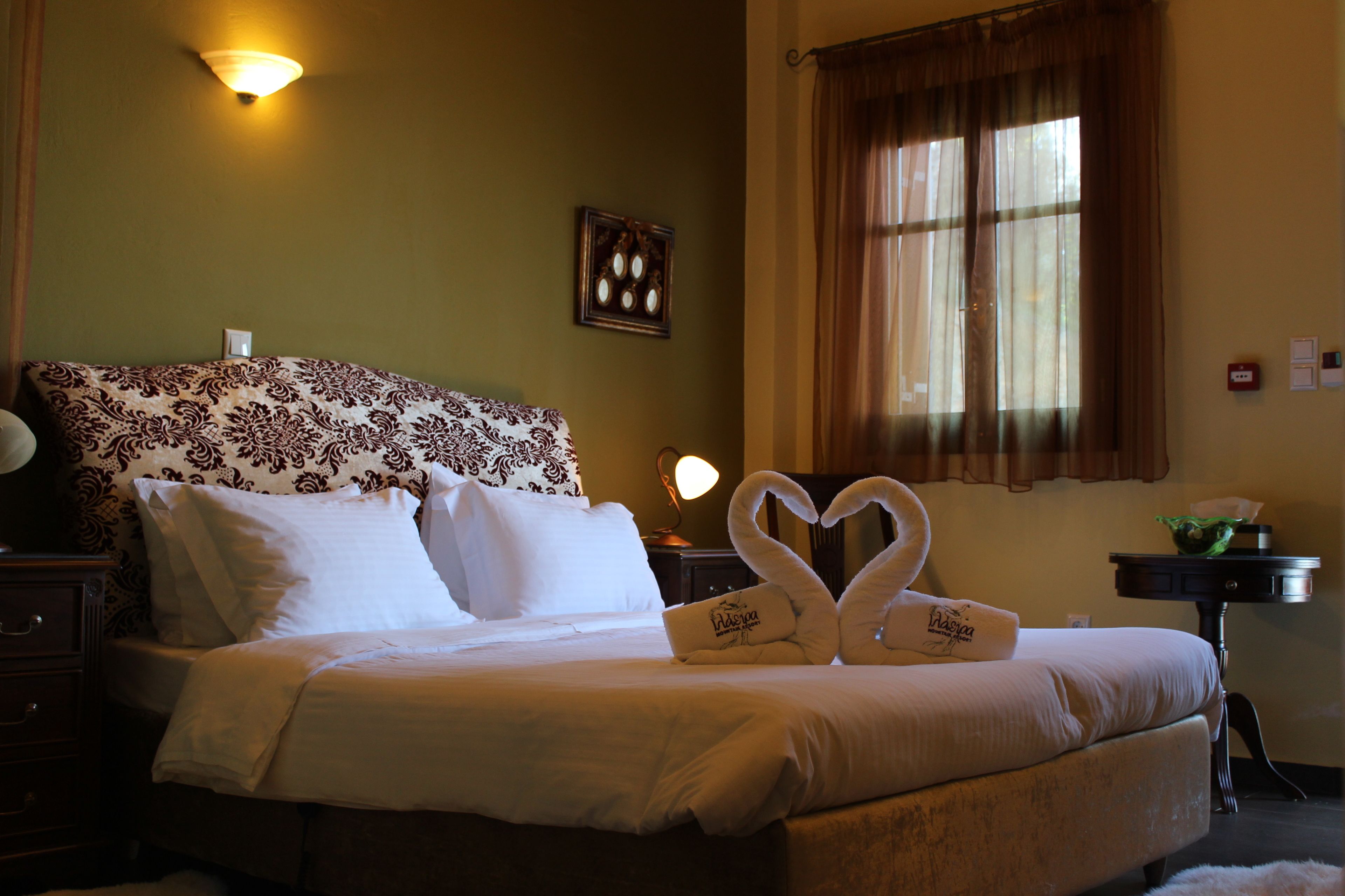 A neatly made bed with white linens and a decorative pillow. There is a wall-mounted light fixture above the bed and a framed picture on the wall.