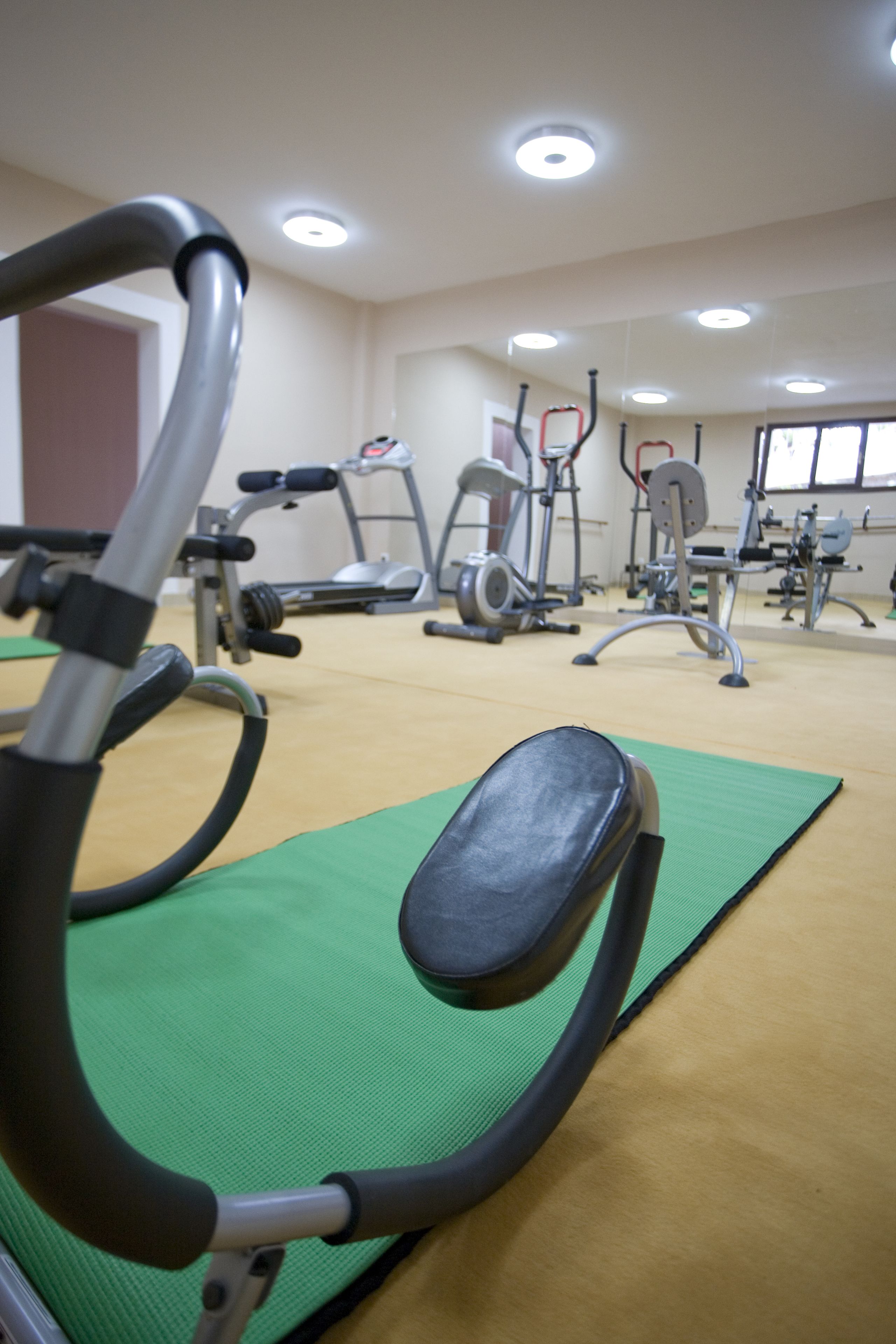 A gym with exercise equipment, green mats, and a ceiling with recessed lighting.