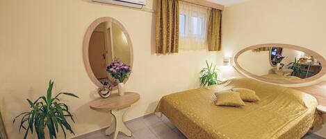 Habitación de hotel con cama, espejo redondo, mesita con un florero y planta en maceta.