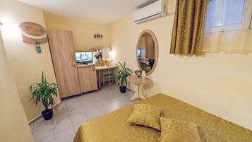 A hotel room with a bed, desk, chair, potted plants, and a mirror.