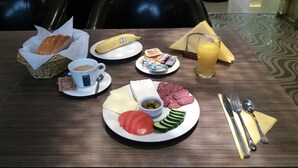 A breakfast setting with a plate of sliced tomatoes, cucumbers, and olives, a banana, a glass of orange juice, and a cup of coffee. - Hotel Color (Varna)