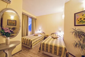 A hotel room with two beds, a round mirror, a small table with a vase of flowers, and a potted plant. - Hotel Color (Varna)