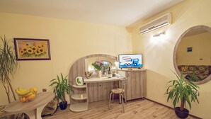 A compact living space with a dining table, a small kitchen area, a television, and potted plants. - Hotel Color (Varna)