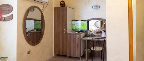 A compact room with a bed, a desk with a computer, a mirror, and an air conditioner.