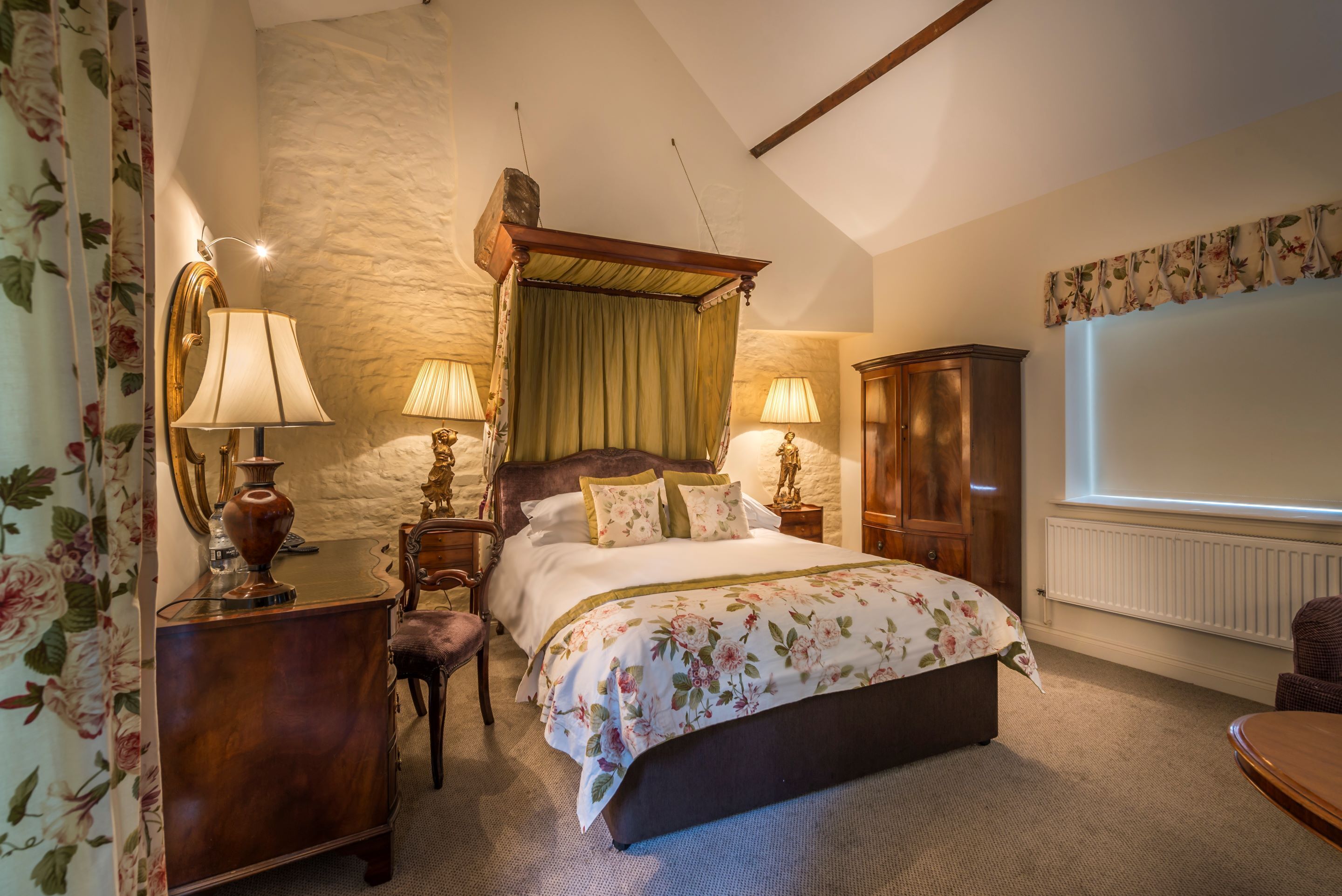 A bedroom with a large bed, two bedside lamps, a wooden wardrobe, and a floral curtain.