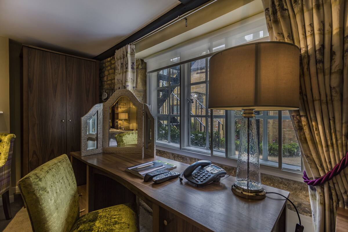 A hotel room with a wooden desk, a telephone, a lamp, and a view of the outside through large windows.