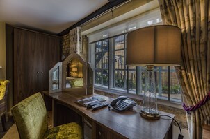 A hotel room with a wooden desk, a telephone, a lamp, and a view of the outside through large windows.