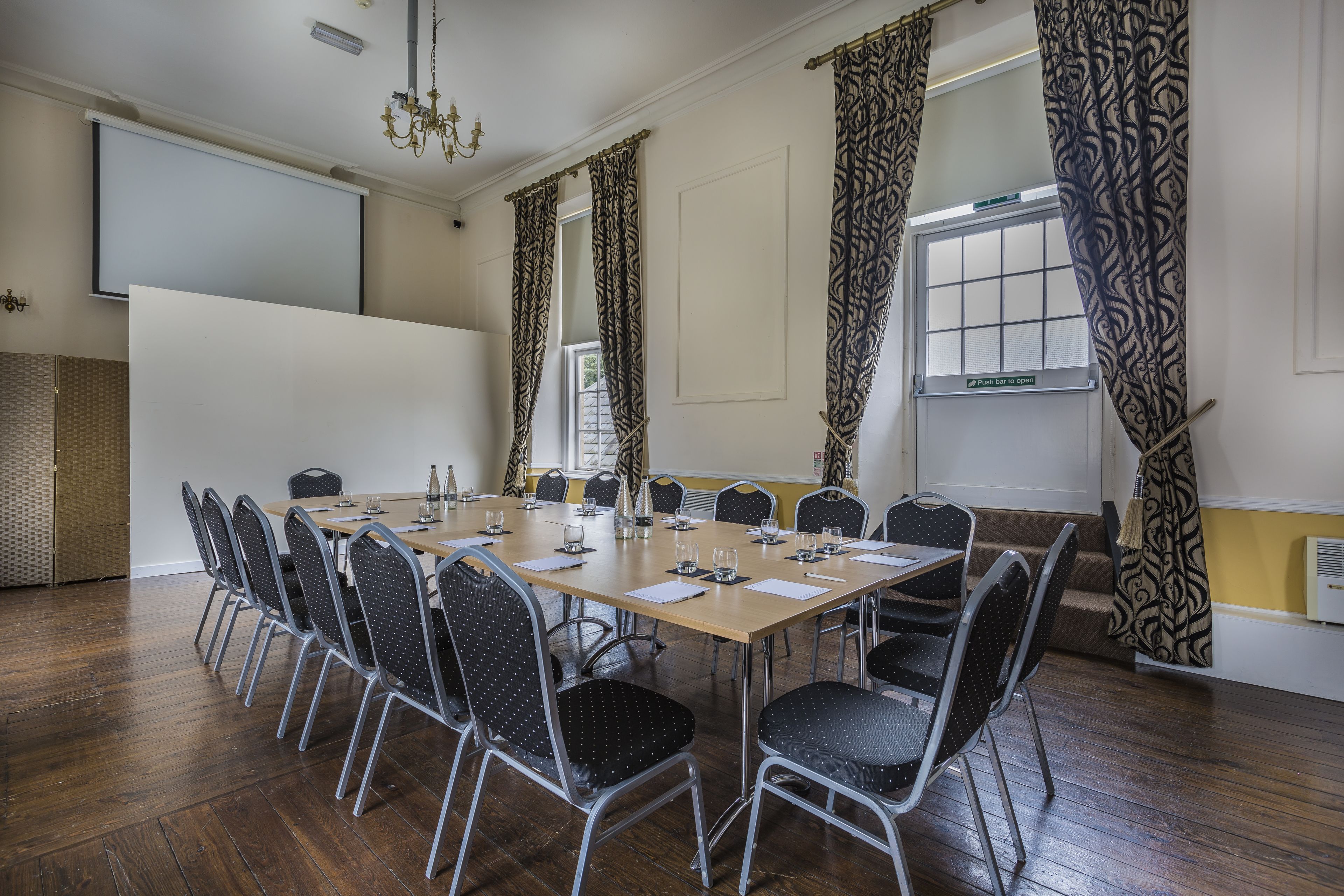 A conference room with a long table, chairs, and a projector screen.