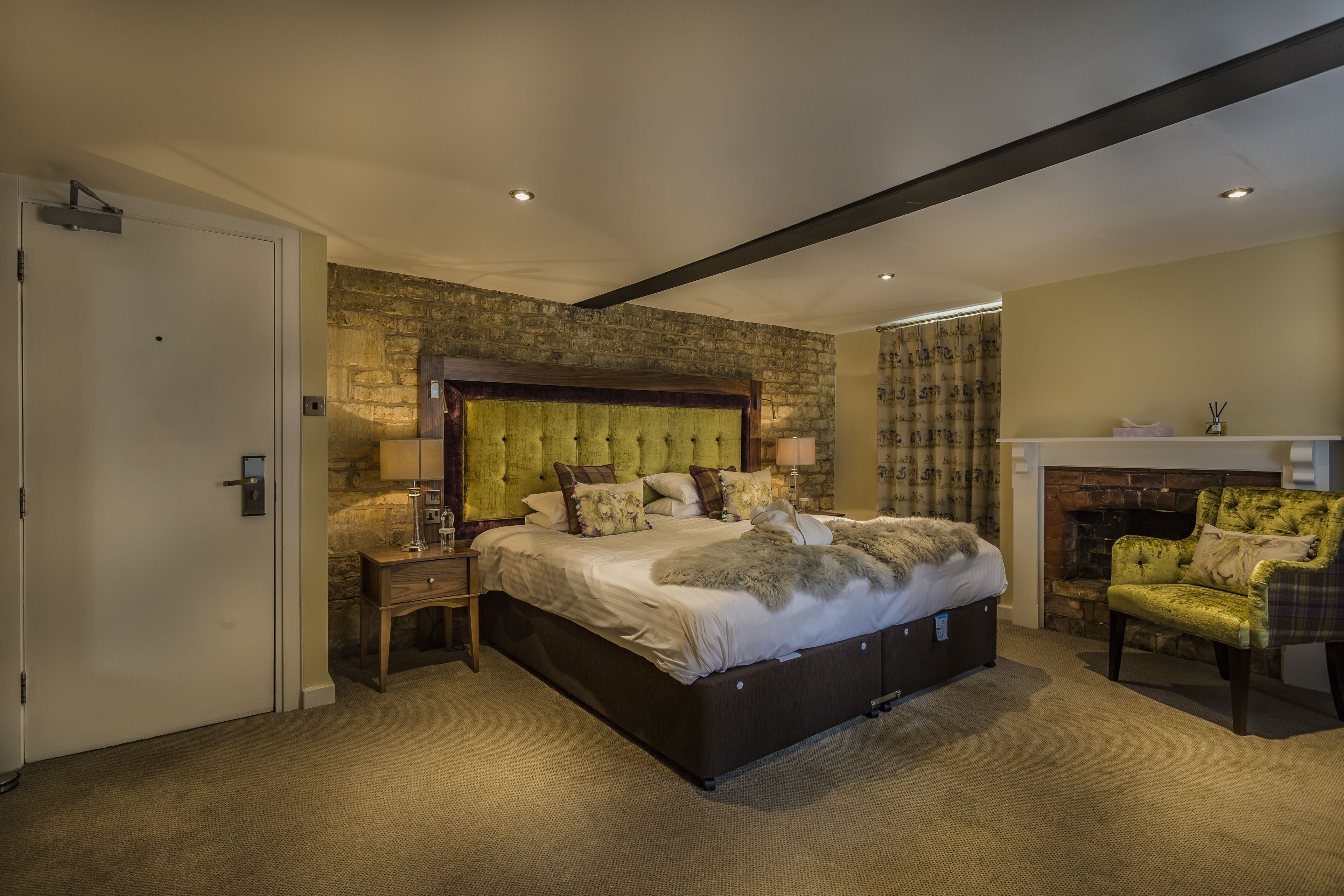 A bedroom with a large bed, a stone accent wall, a fireplace, and a cozy chair.