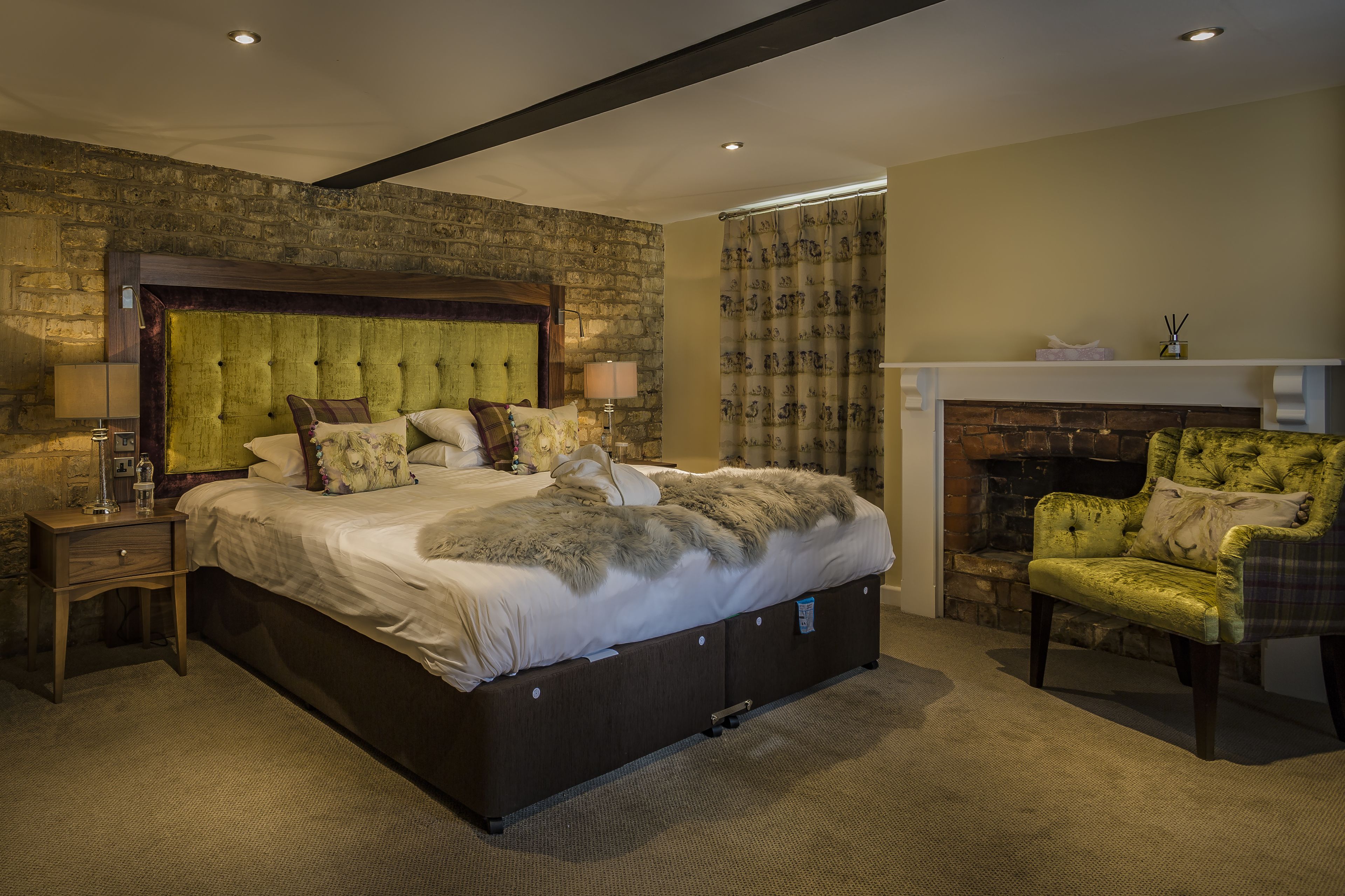 A bedroom with a large bed, a nightstand, a chair, a fireplace, and a stone wall.