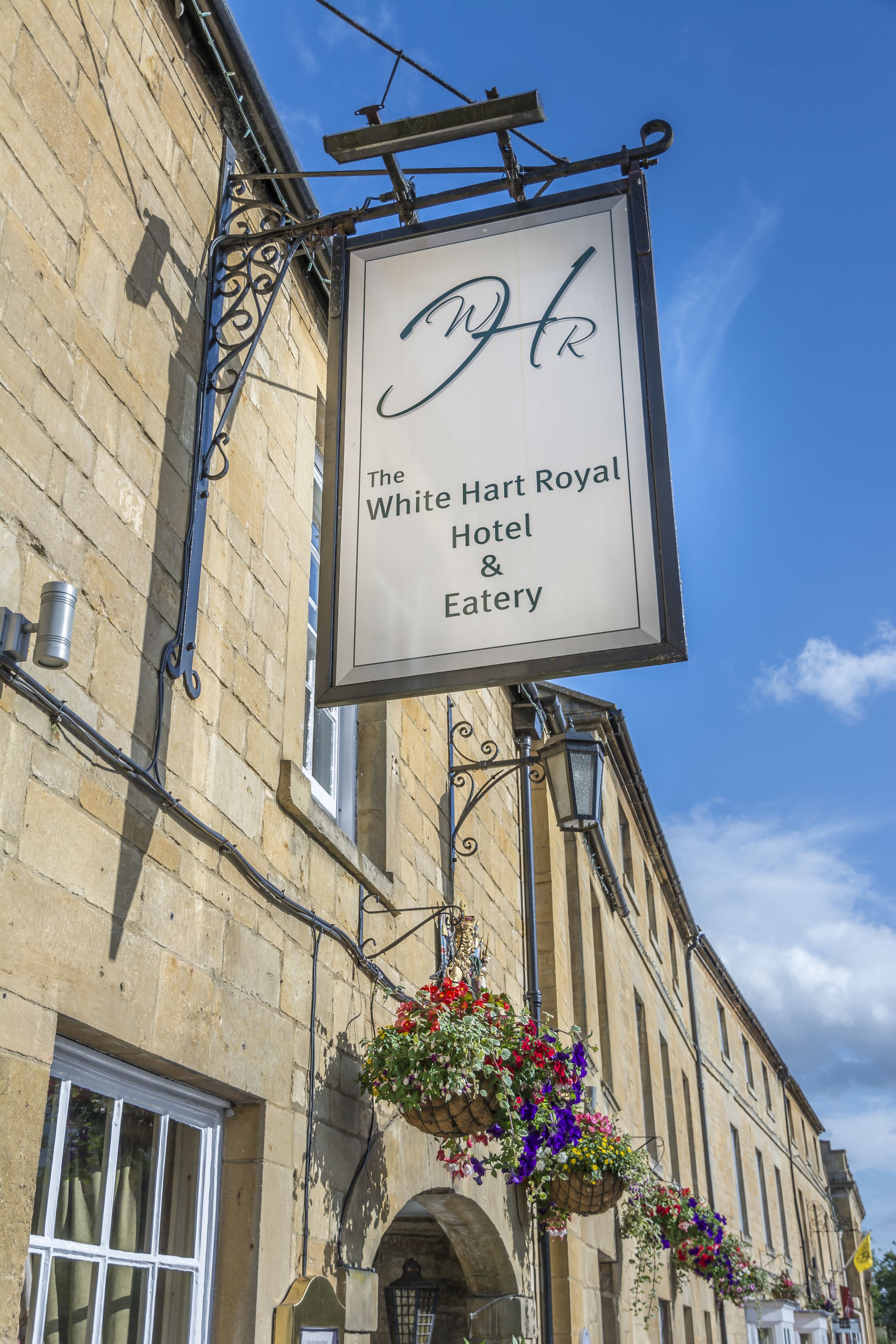 A sign for The White Hart Royal Hotel & Eatery, featuring a traditional hanging sign with a clear view of the building's architecture and a clear blue sky in the background.