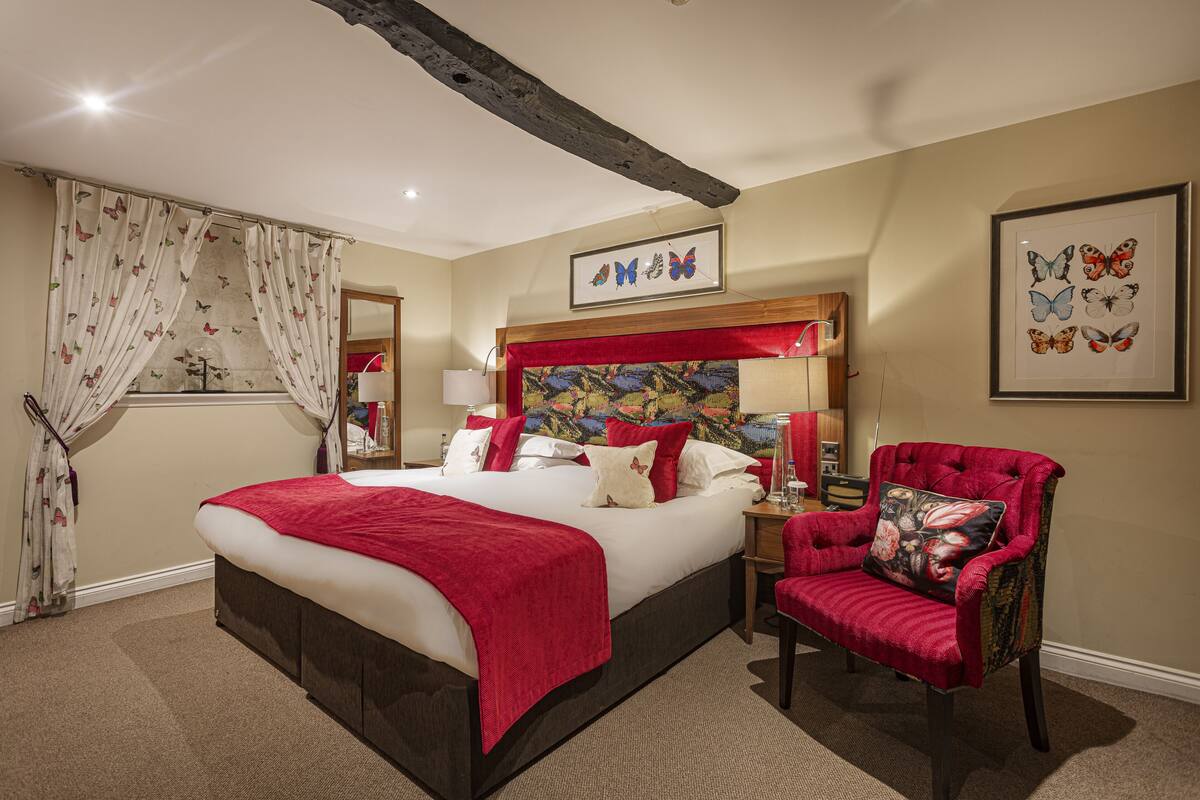 A well-appointed bedroom with a large bed, a red upholstered chair, and a headboard with a colorful tapestry.