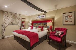 Un dormitorio elegante con una cama grande, un sillón tapizado en rojo y un cabecero con un tapiz colorido.