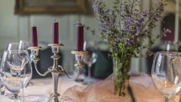 A table with three candles on a candelabra, a vase with purple flowers, and several wine glasses.
