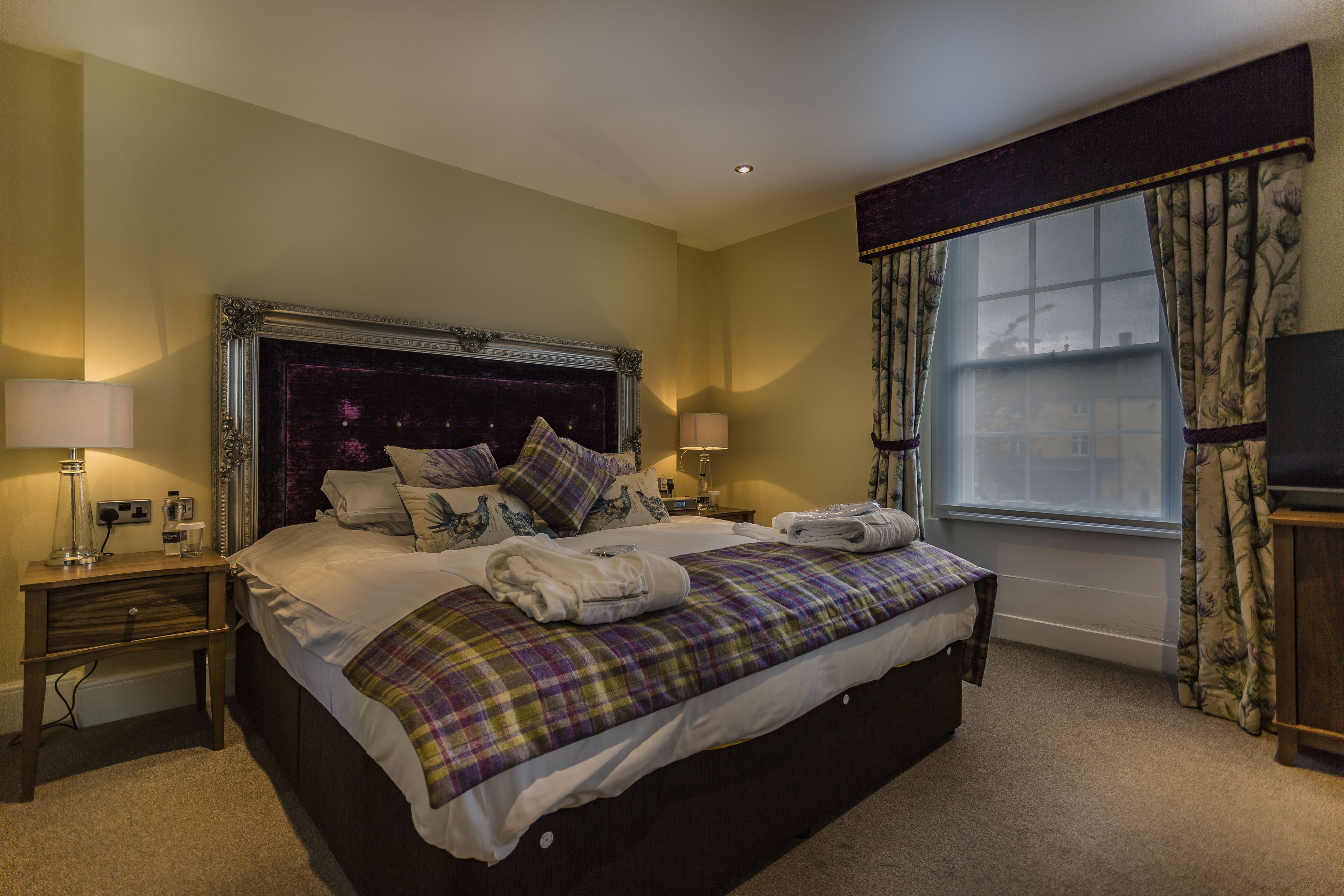 A neatly made bed with a plaid blanket, a dark headboard, and two bedside lamps.