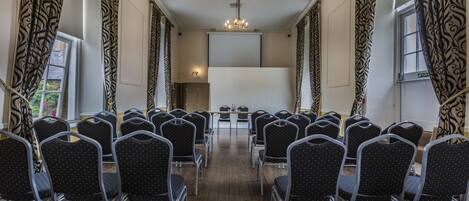 A conference room with rows of chairs facing a whiteboard, a chandelier, and patterned curtains.