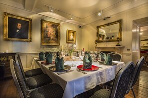 Un comedor formal con una mesa dispuesta para cuatro personas, retratos enmarcados en las paredes y un espejo sobre la mesa.