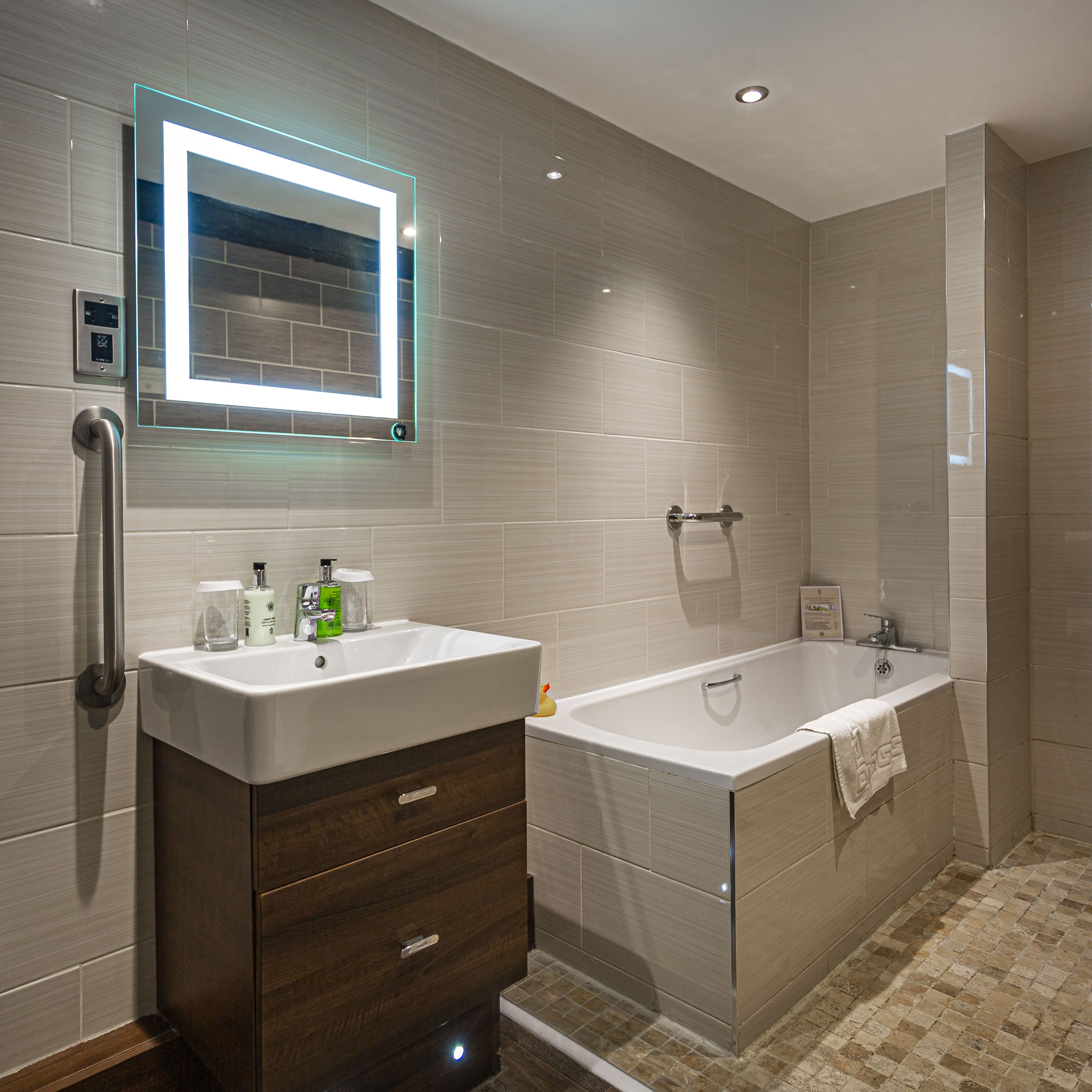 A modern bathroom with a vanity, a large bathtub, and a mirror with illuminated edges.