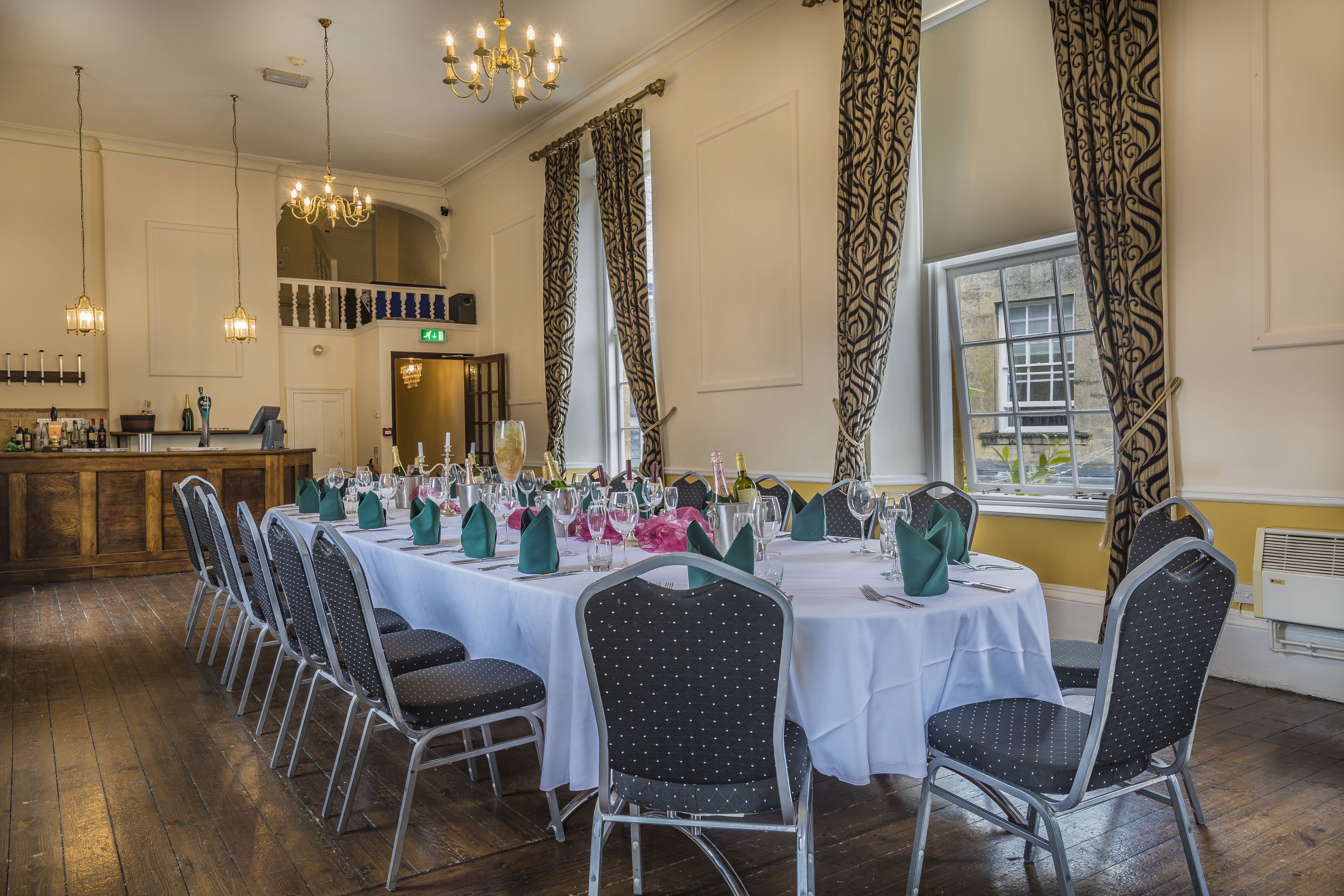 A dining area with multiple tables set for a formal event, featuring chandeliers and patterned curtains.