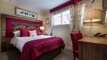 A hotel room with a bed, a desk, a chair, a lamp, and a window with curtains.