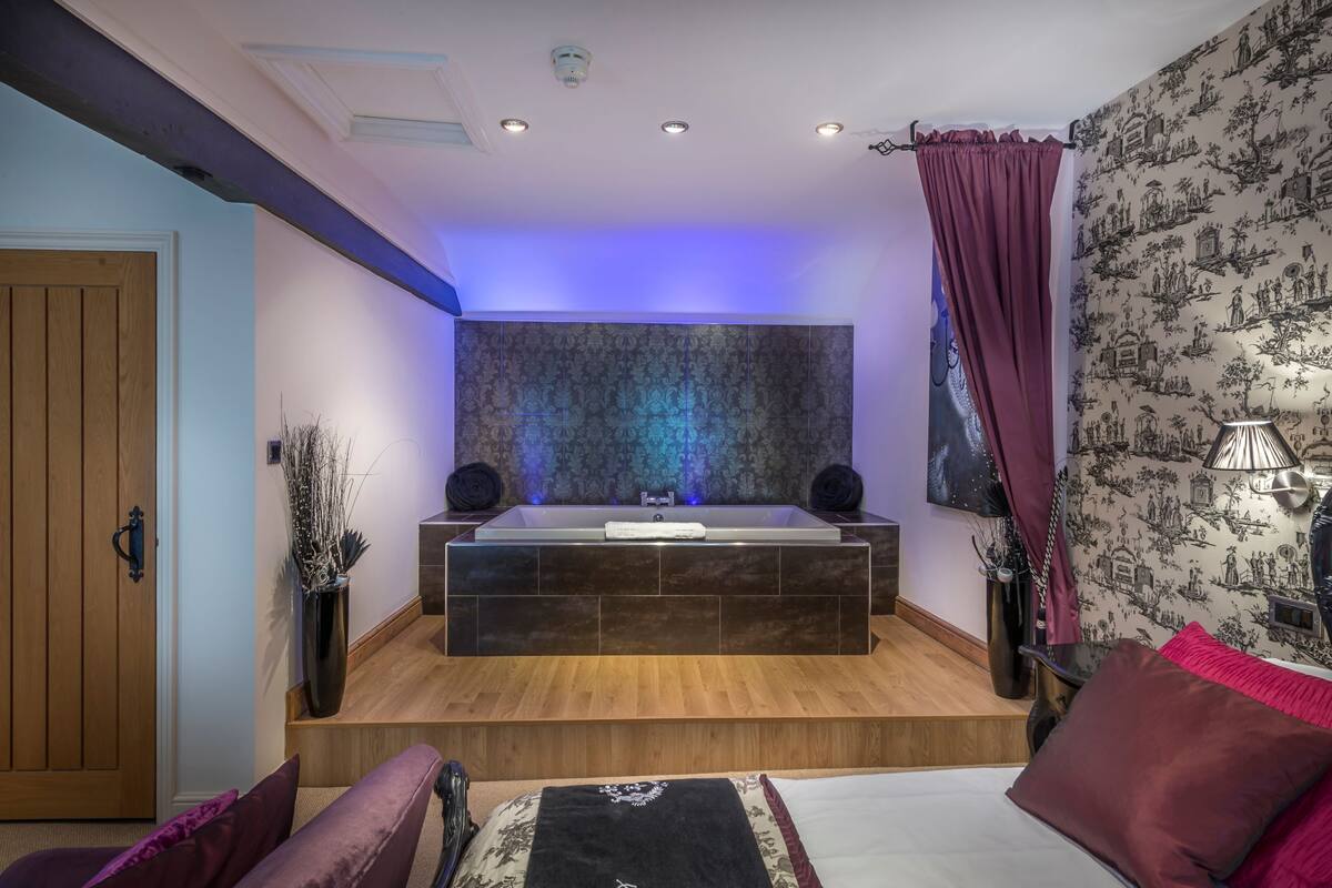 A modern bathroom with a large bathtub, wooden flooring, and a decorative wall.