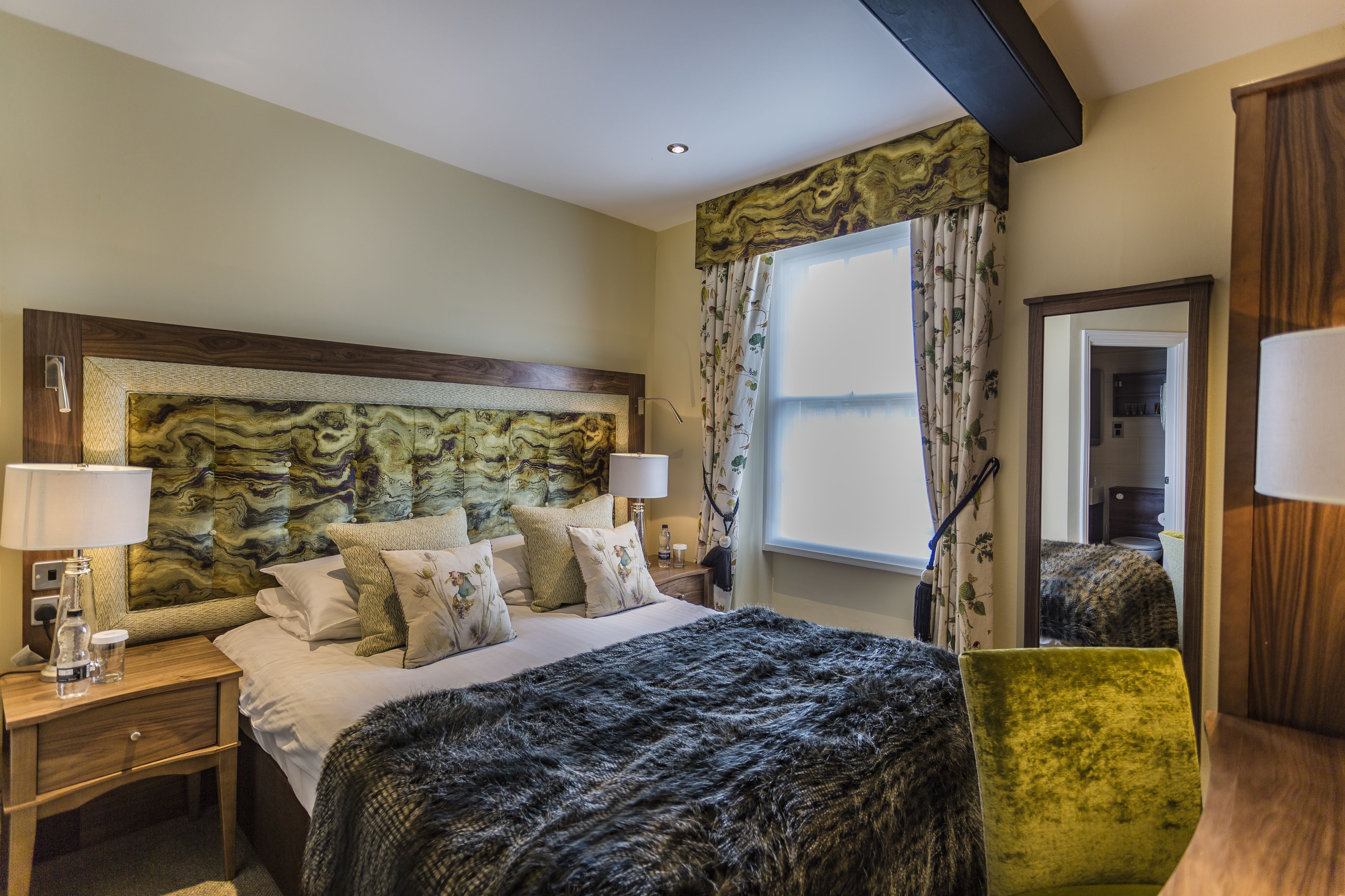 A hotel room with a large bed, a green chair, a wooden headboard, and a window with curtains.