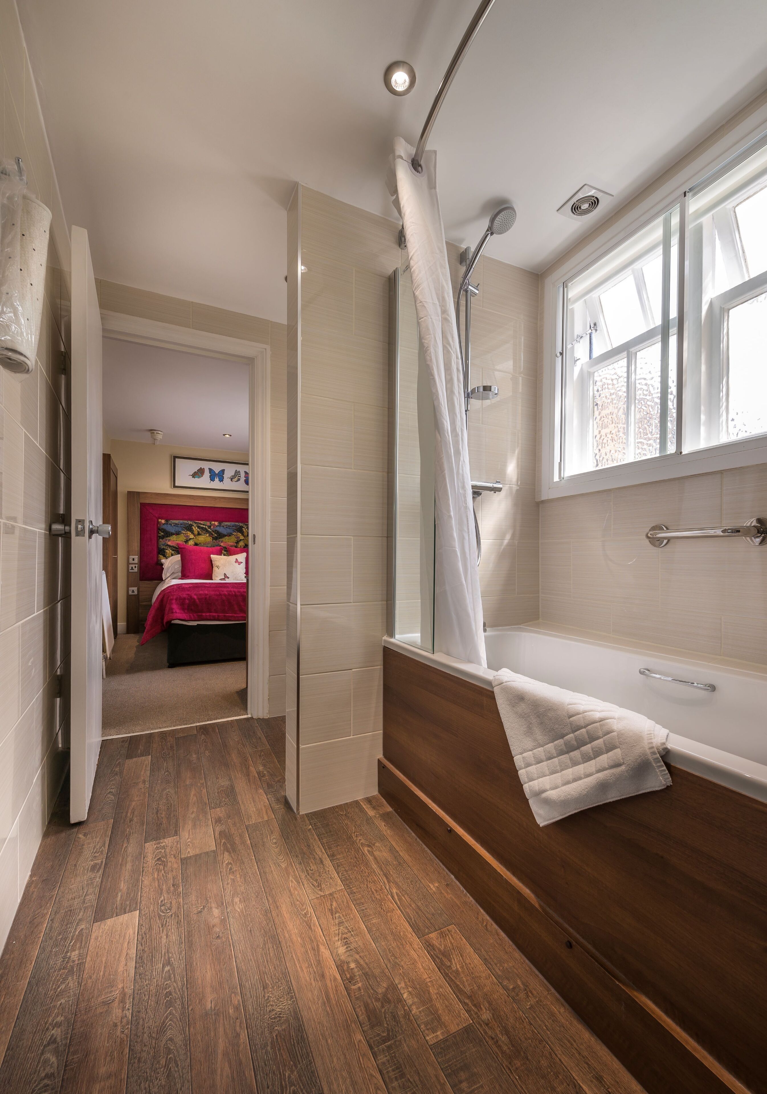 A modern bathroom with a walk-in shower, a bathtub, and a wooden floor.