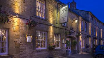 A stone building with a sign for The White Hart Royal Hotel & Eatery, featuring multiple windows, flower boxes, and a parked car.