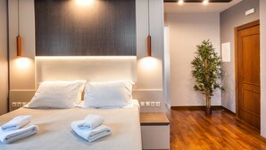 Ein Hotelzimmer mit einem großen Bett, zwei Nachttischlampen, einem Holz-Kopfstück, einer Topfpflanze und einer Holztür.