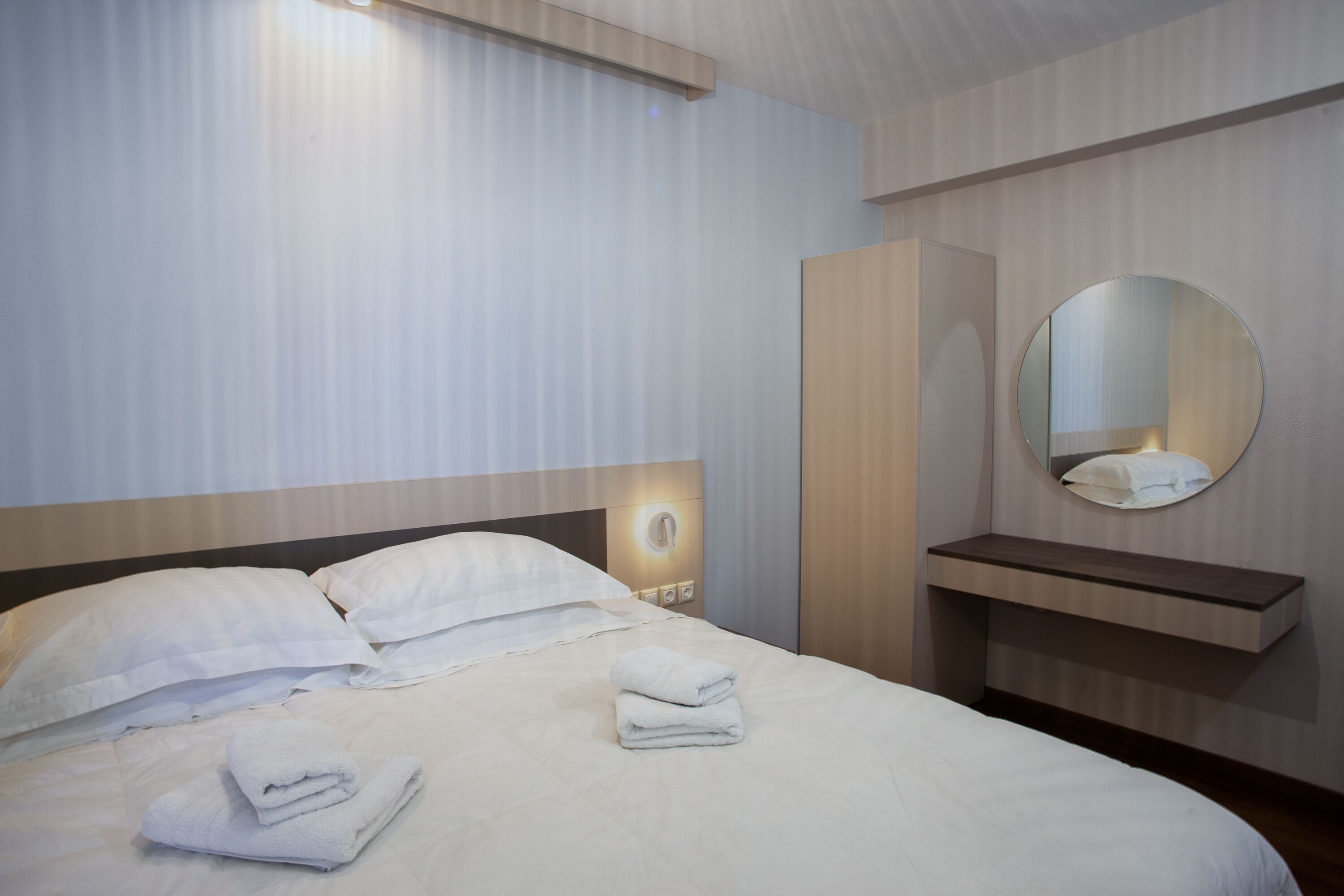 Una habitación de hotel con una cama bien hecha, una mesita de noche, un espejo y una repisa en la pared.