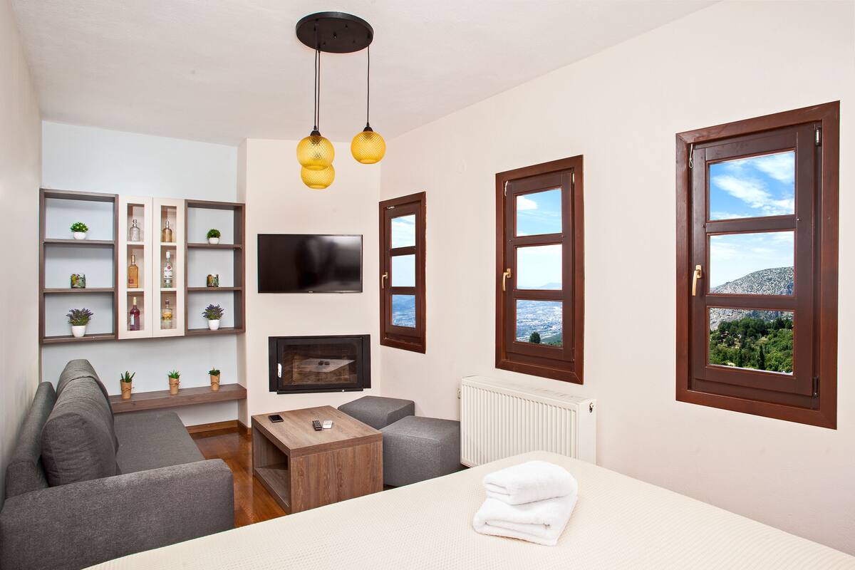 A modern hotel room with a sofa, a TV, a wooden coffee table, and a bed with a neatly folded towel.