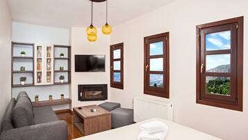 A modern hotel room with a sofa, a TV, a wooden coffee table, and a bed with a neatly folded towel.